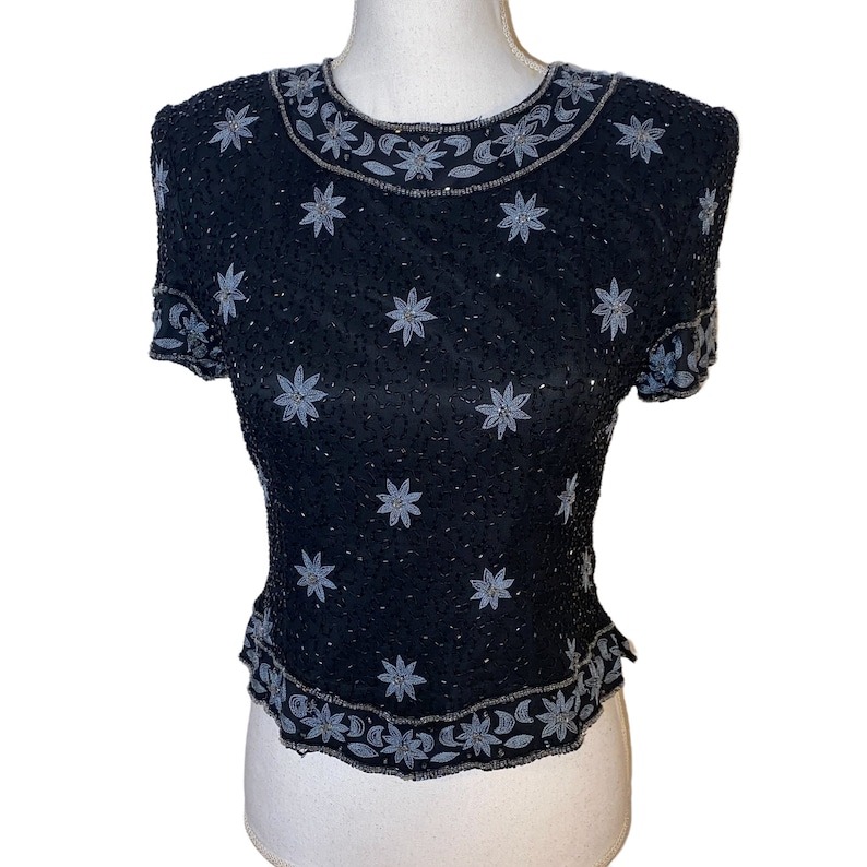 May include: A black sequined top with a silver floral design. The top has short sleeves and a round neckline.