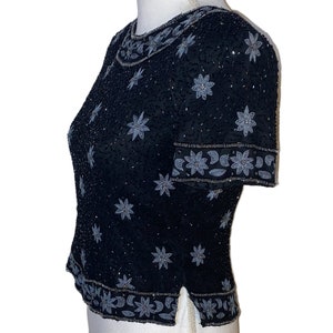 May include: A black sequined top with silver floral embroidery. The top has short sleeves and a round neckline.