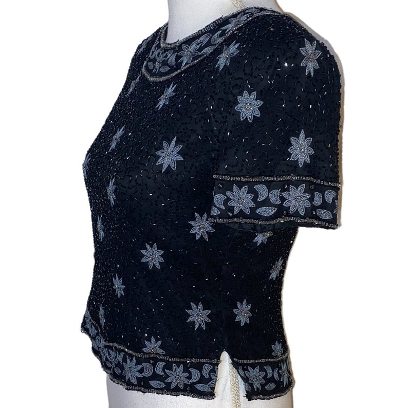 May include: A black sequined top with silver floral embroidery. The top has short sleeves and a round neckline.
