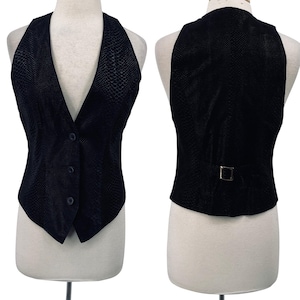 Könnte beinhalten: Eine schwarze Neckholder-Weste mit strukturiertem Schlangenmuster. Die Weste hat einen V-Ausschnitt, drei Knöpfe und einen Schnallenverschluss auf der Rückseite. Die Weste wird auf einer Schaufensterpuppe präsentiert.