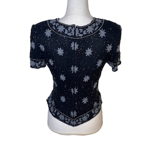 May include: A black beaded top with a silver floral design. The top has short sleeves and a fitted silhouette.