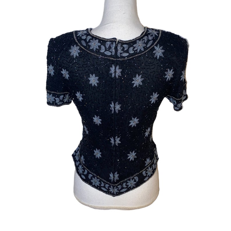 May include: A black beaded top with a silver floral design. The top has short sleeves and a fitted silhouette.