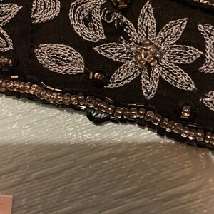 May include: Close-up of a black fabric with silver embroidery of flowers and leaves. The fabric is trimmed with a row of small, clear beads.