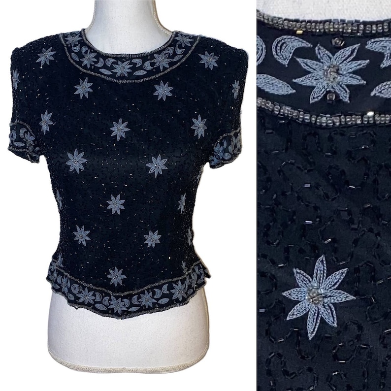 May include: A black sequined top with a silver floral design. The top has short sleeves and a round neckline.