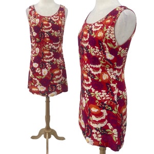 May include: A sleeveless red mini dress with a floral print featuring white, orange, and green flowers. The dress has a scoop neck and a straight silhouette.