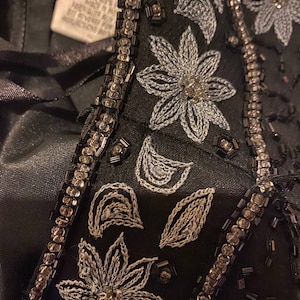 May include: Close-up of a black fabric with silver and black beading and embroidery. The embroidery features a floral design with leaves and flowers.