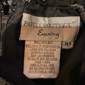 May include: A black silk evening dress with beaded embellishments. The label reads "Papell Boutique Evening" and includes details about the fabric and care instructions.