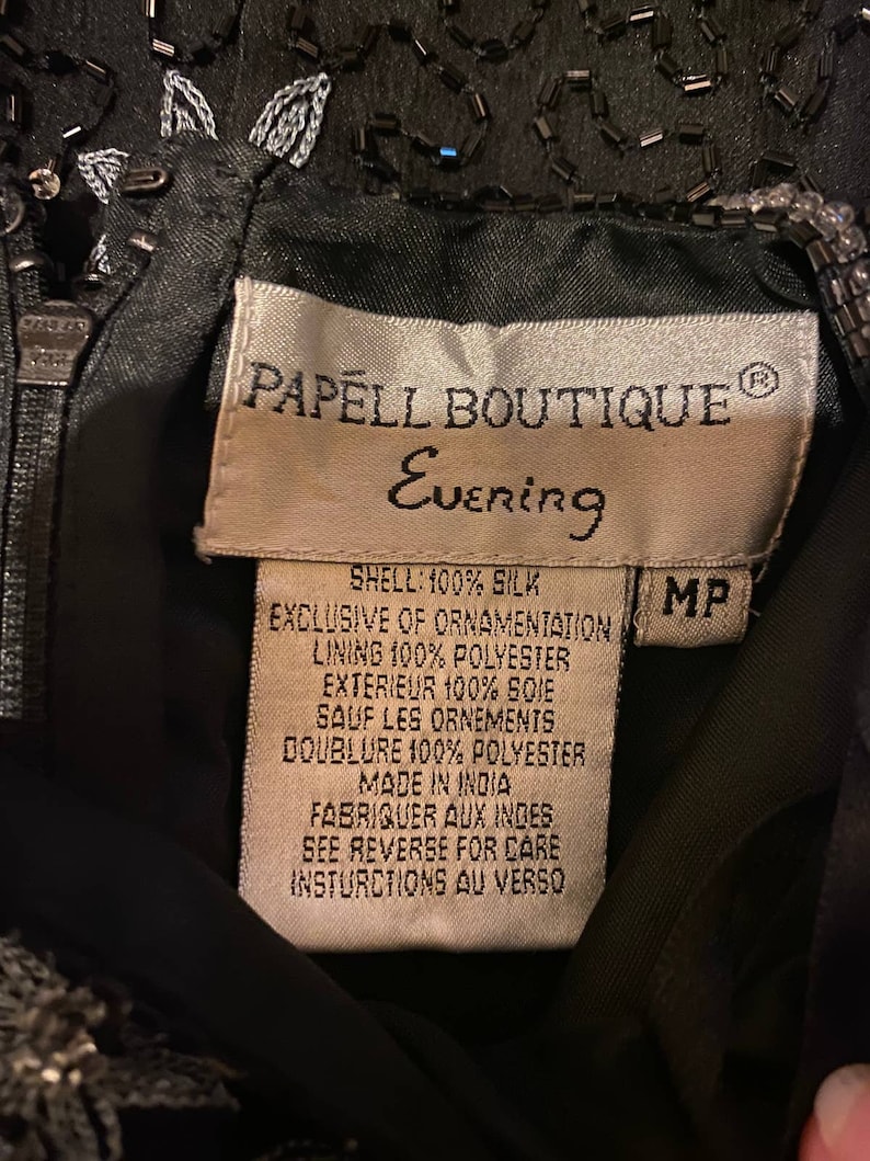 May include: A black silk evening dress with beaded embellishments. The label reads "Papell Boutique Evening" and includes details about the fabric and care instructions.