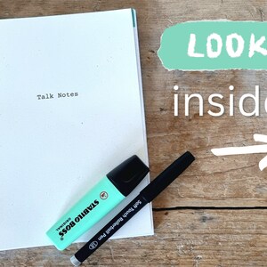 May include: A white spiral bound notebook with the words "Talk Notes" printed on the front cover. A turquoise highlighter and a black pen are lying on top of the notebook.
