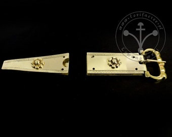 May include: A gold-colored metal buckle with a floral design. The buckle is composed of two parts: a triangular piece and a rectangular piece with a hook. The pieces are connected by a hinge. The buckle has a decorative border.