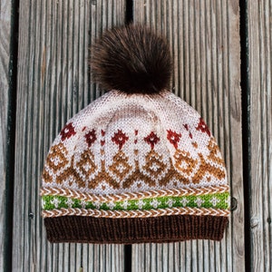 May include: A brown, white, and green knitted hat with a brown pom-pom on top. The hat has a geometric pattern.