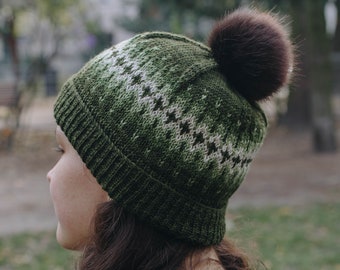 May include: A green knit beanie with a white geometric pattern and a brown faux fur pom pom.