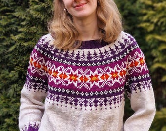 May include: A beige knit sweater with a geometric pattern in purple, orange, and white. The sweater has a crew neck and long sleeves with purple cuffs. The design features star-like shapes and bands of color.