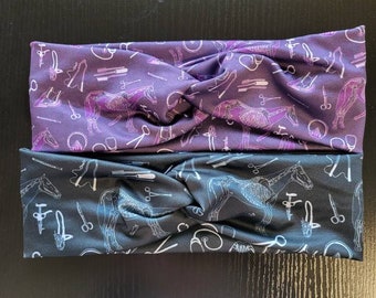 May include: Two fabric headbands with a horse skeleton and veterinary tools pattern. The top headband is purple and the bottom headband is black.