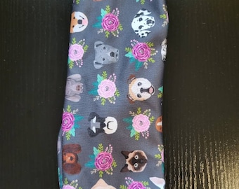 May include: A gray headband with a repeating pattern of dog faces and floral designs. The dogs are of various breeds and colors, and the flowers are pink and purple.