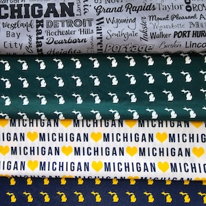 May include: A collage of three fabric swatches featuring different patterns of the state of Michigan. The top swatch is green with white outlines of the state. The middle swatch is white with the words "Michigan" repeated and a yellow heart between each word. The bottom swatch is navy blue with yellow outlines of the state.