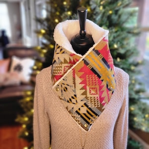 May include: A warm, cozy neck warmer with a geometric pattern in shades of red, yellow, and blue. The neck warmer is lined with white faux fur.