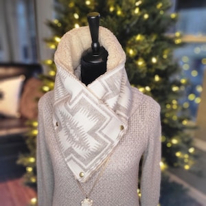 May include: A gray and white patterned cowl neck scarf with a sherpa lining. The scarf is worn on a mannequin with a gray sweater.