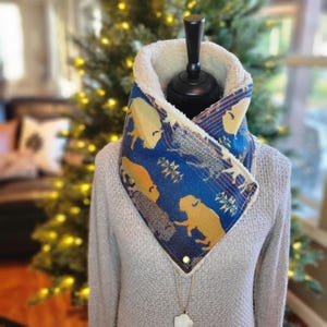 May include: A blue and brown patterned fleece neck warmer with a sherpa lining. The neck warmer features a geometric pattern with animal silhouettes.