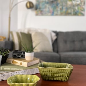 May include: Two green ceramic planters, one with a wavy rim and the other with a rectangular shape and a textured design. The planters are on a wooden table.