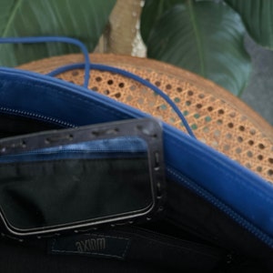May include: The inside of a blue leather bag with a black zipper and a black pocket with the word "Axiom" printed on it.