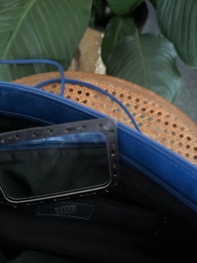 May include: The inside of a blue leather bag with a black zipper and a black pocket with the word "Axiom" printed on it.