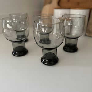 May include: Four clear glass tumblers with black bases. The glasses are empty and sitting on a white surface.