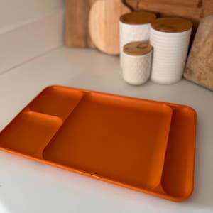 May include: An orange plastic divided serving tray with three sections. The tray is on a white surface.