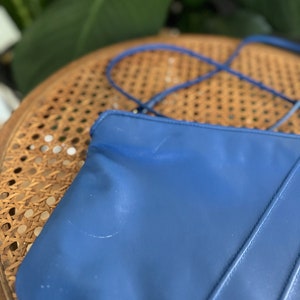 May include: A blue leather tote bag with a single strap. The bag has a smooth, slightly textured surface and is sitting on a woven chair.