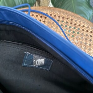 May include: Inside of a blue bag with a black zipper and a black fabric lining. The bag has a label that says "axiom" in white lettering.
