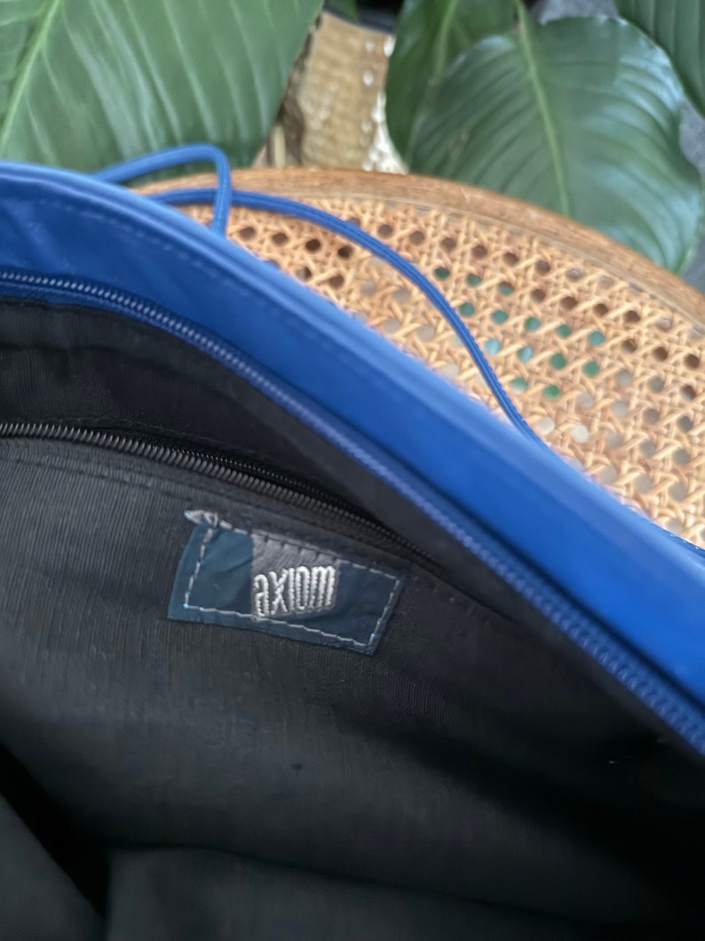 May include: Inside of a blue bag with a black zipper and a black fabric lining. The bag has a label that says "axiom" in white lettering.