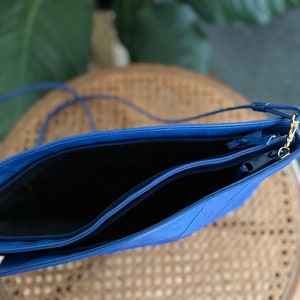 May include: A blue leather crossbody bag with two zippered compartments. The bag has a gold zipper pull and a long strap.