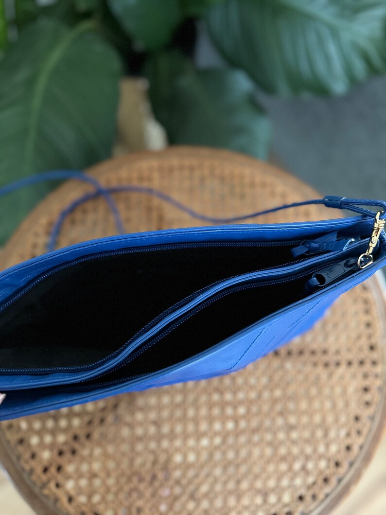May include: A blue leather crossbody bag with two zippered compartments. The bag has a gold zipper pull and a long strap.