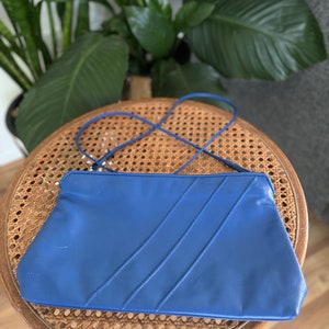 May include: A blue leather clutch purse with a long strap. The purse has a flap closure and three stitched lines on the front.