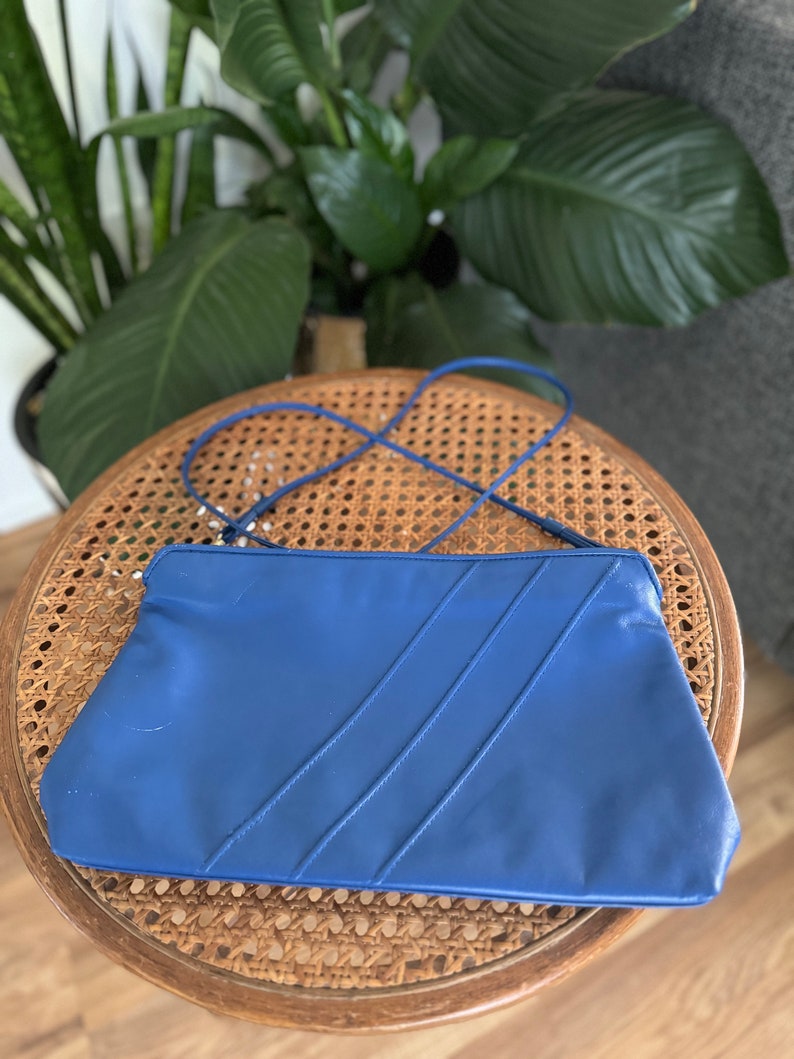 May include: A blue leather clutch purse with a long strap. The purse has a flap closure and three stitched lines on the front.