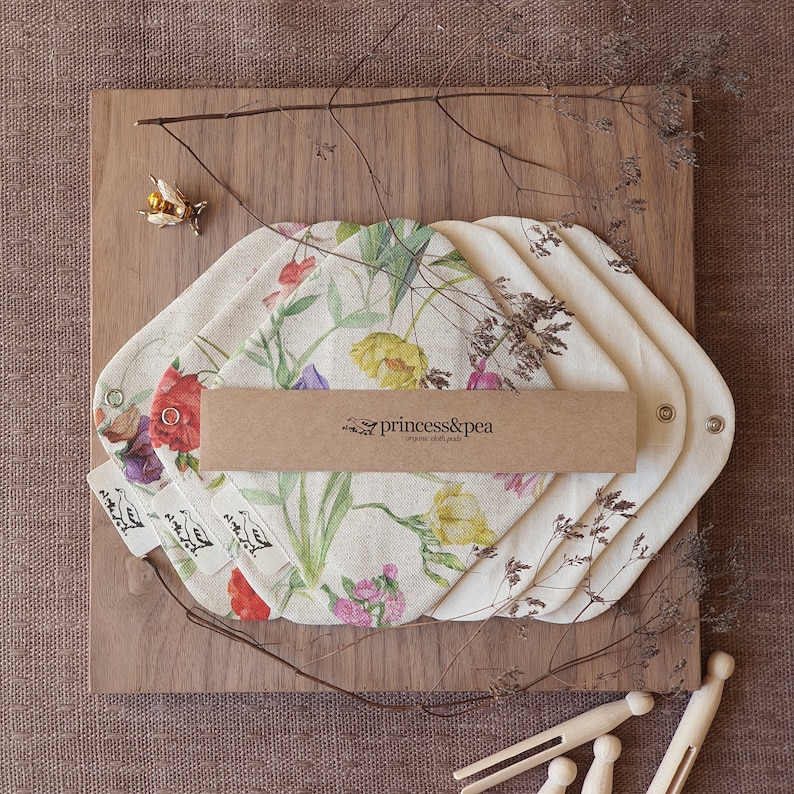 May include: Set of four organic cloth pads with a floral print featuring yellow, pink, and purple flowers. The pads are packaged with a brown paper label that reads "princess&pea organic cloth pads".