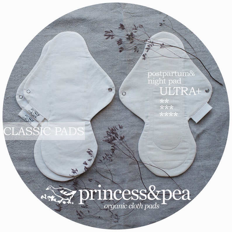 May include: Two organic cotton reusable cloth pads. One is a classic pad and the other is an ultra plus postpartum and night pad. The pads are white and have a light gray background. The text "CLASSIC PADS" is printed on the left pad. The text "postpartum & night pad ULTRA+ *** ****" is printed on the right pad. The text "princess&pea organic cloth pads" is printed below the pads.
