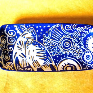 Peut inclure: Un plat en céramique bleu avec un motif blanc de poissons stylisés et de volutes. Le plat a un glaçage bleu moucheté.