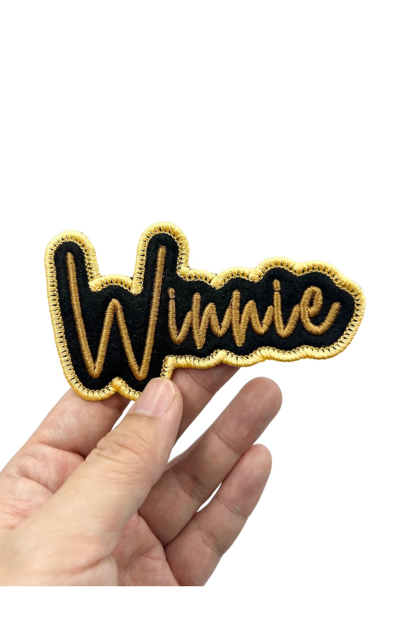 May include: A black felt patch with gold embroidered lettering that reads "Winnie".