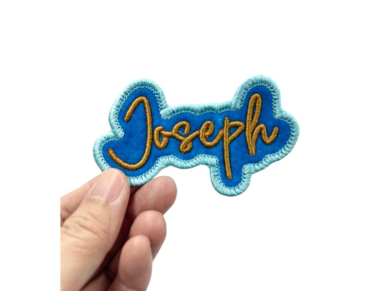 May include: A blue felt patch with a gold embroidered name "Joseph" in a cursive font.