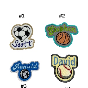 May include: Four embroidered patches featuring different sports themes. The first patch is a heart with a football and the name "Scott". The second patch has a basketball and the name "Stephen". The third patch has a football and the name "Ronald". The fourth patch has a baseball and the name "David".