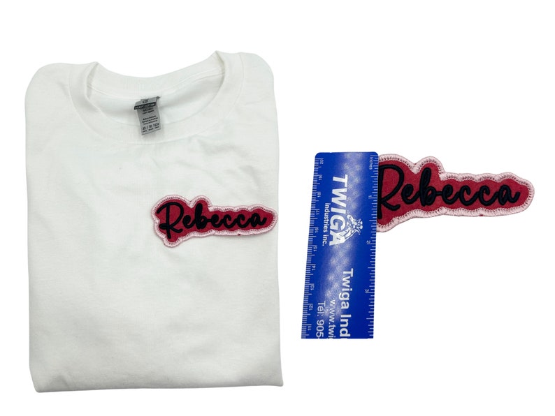 May include: A white t-shirt with a pink and black iron-on patch that says "Rebecca".
