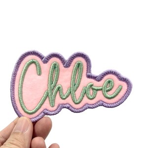 May include: A pink felt patch with a purple outline and green embroidered lettering that reads "Chloe".
