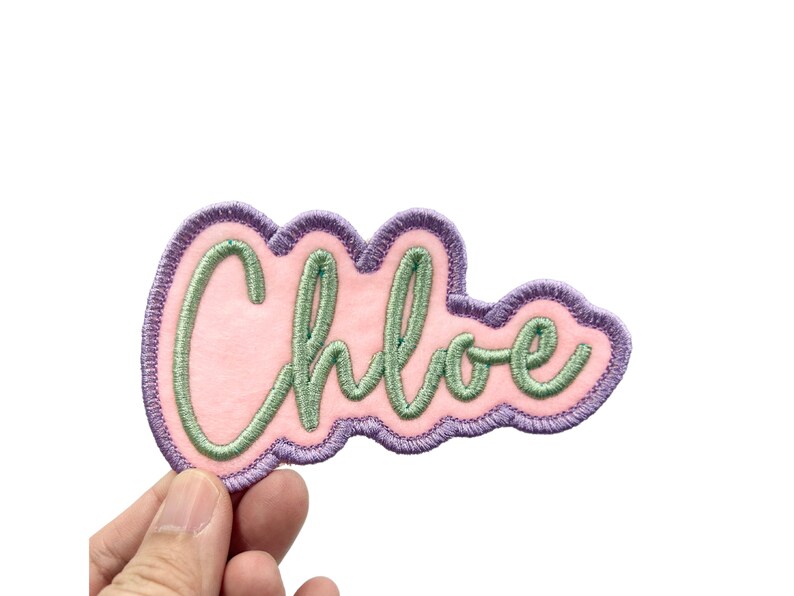 May include: A pink felt patch with a purple outline and green embroidered lettering that reads "Chloe".