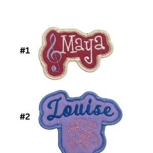 May include: Two embroidered iron-on patches. The first patch is red with a treble clef and the name "Maya" in white. The second patch is purple with the name "Louise" in blue and a pair of pink ballet shoes.