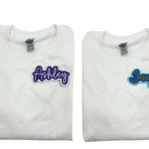 May include: Two white t-shirts with personalized names. The left shirt has a purple "Ashley" patch. The right shirt has a blue "Joseph" patch.