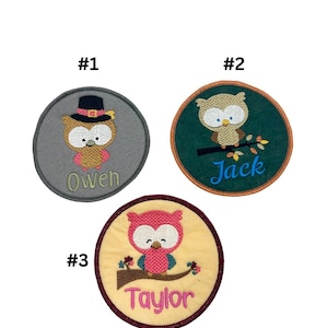 May include: Three round felt patches with embroidered owls and names. The first patch is gray with a brown owl wearing a pilgrim hat and the name "Owen". The second patch is green with a brown owl on a branch and the name "Jack". The third patch is yellow with a pink owl on a branch and the name "Taylor".