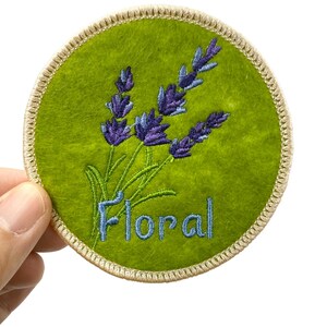 May include: A green felt circular patch with a lavender flower design and the word "Floral" embroidered in blue thread.