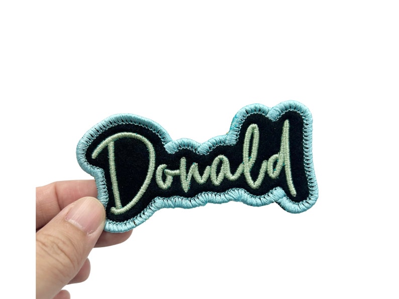 May include: A blue and black embroidered patch with the word "Donald" in white thread.
