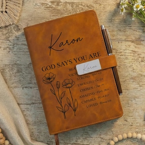 May include: A brown leather journal with the name "Karon" and the phrase "GOD SAYS YOU ARE" printed on the cover. The journal includes a pen holder with a pen, floral illustrations, and inspirational words.